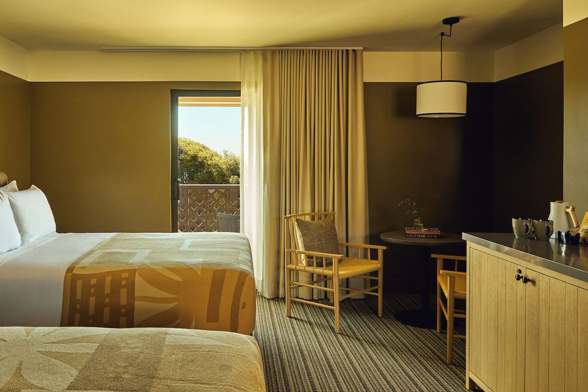 Une chambre d’hôtel avec deux lits, un bureau, une chaise, une télévision et une fenêtre avec des rideaux.