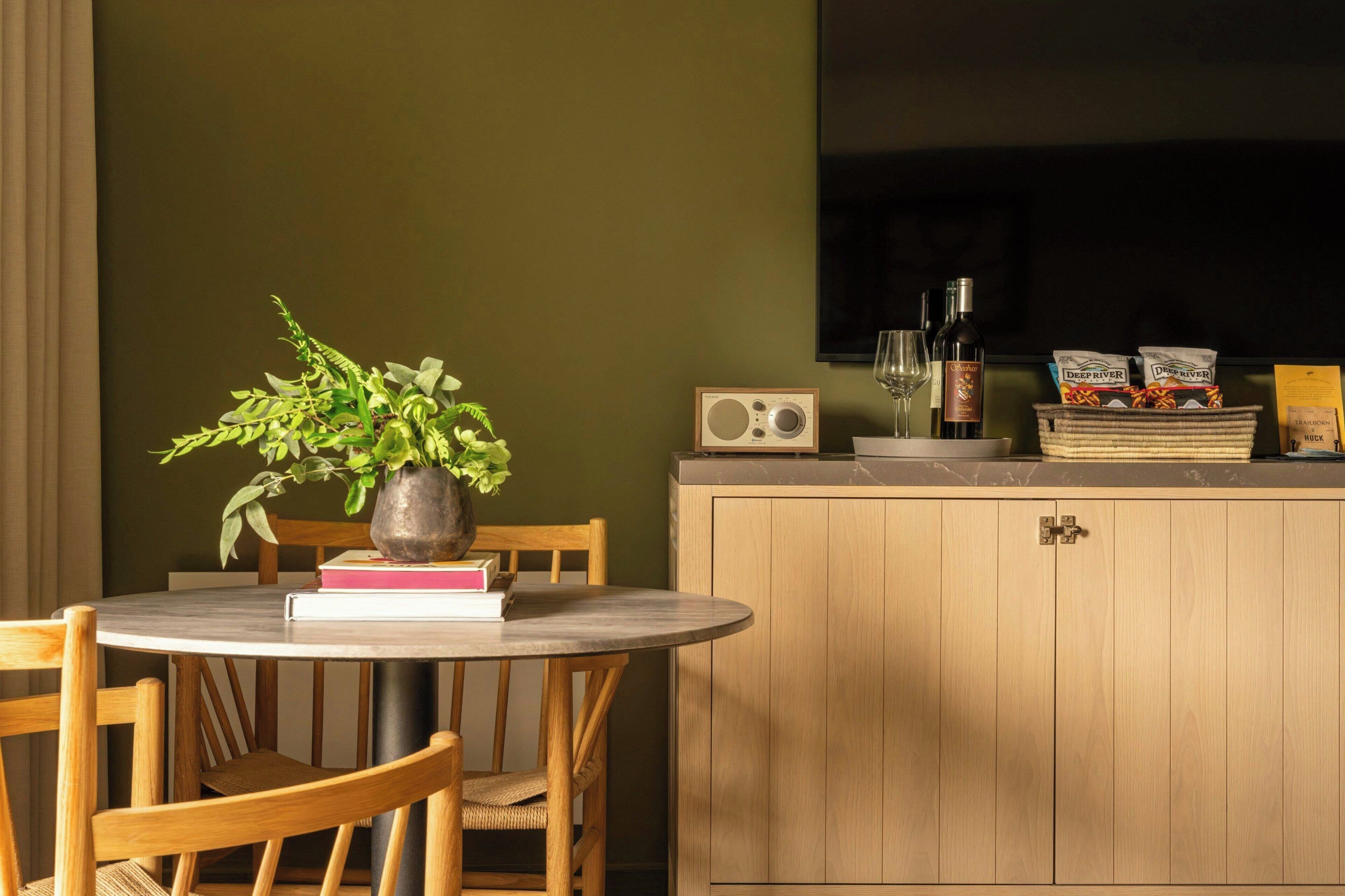 A dining area with a round table, chairs, a potted plant, a radio, wine glasses, and a cabinet.