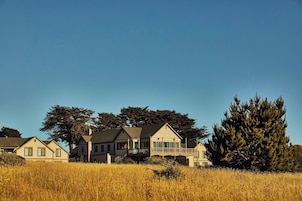 A large house with a balcony, surrounded by tall trees and a field.