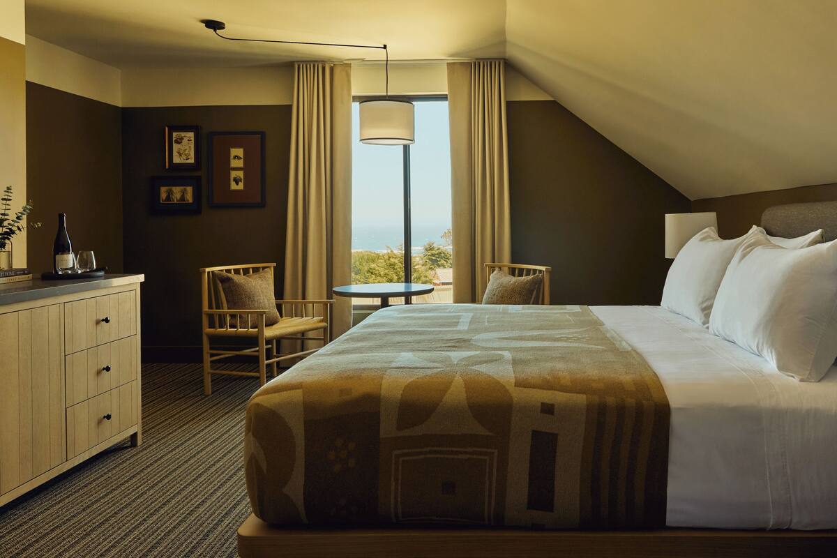 Une chambre d’hôtel équipée d’un lit, d’un bureau, d’une chaise, d’une lampe et offrant une vue sur l’extérieur.