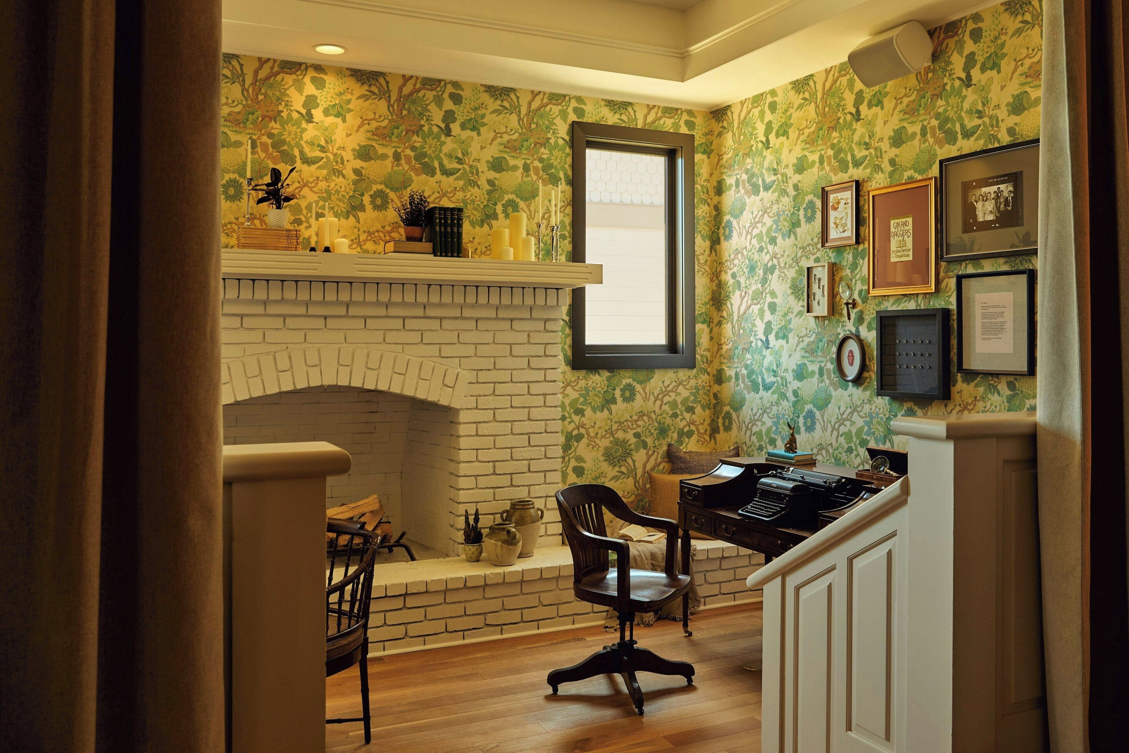 A room with a brick fireplace, a desk with a typewriter, and a window with a view.