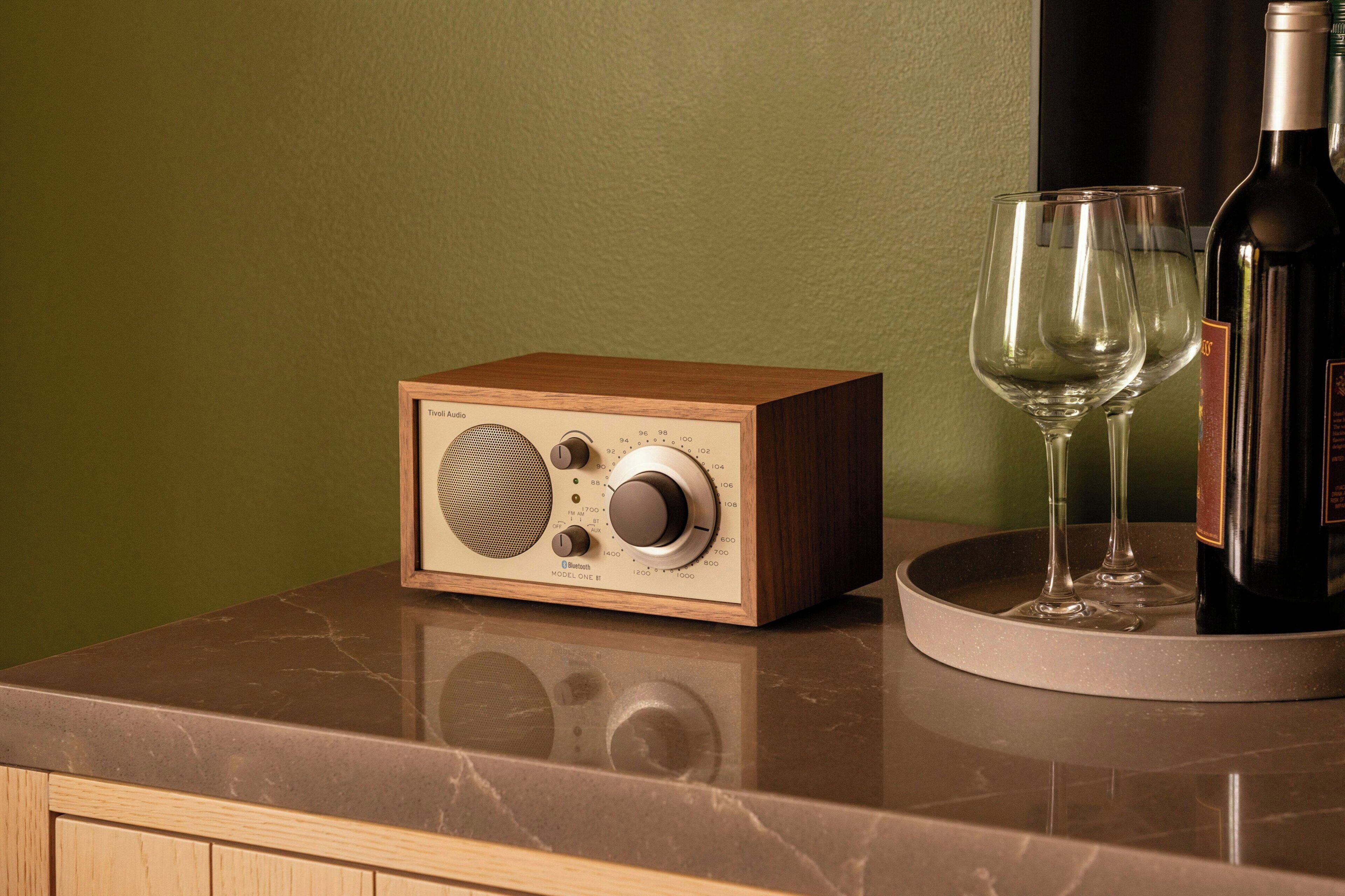 A wooden radio on a marble countertop with two wine glasses and a bottle.