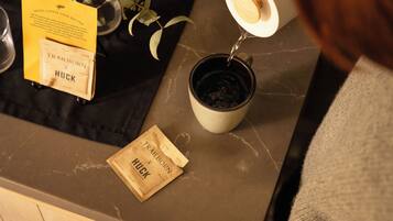 A coffee mug on a counter with a packet of coffee labeled 'Trailborn HUCK' and a yellow sign with text.