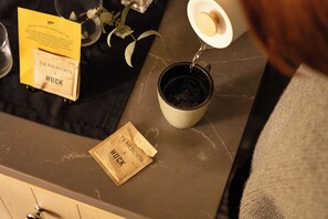 Eine Kaffeetasse auf einer Arbeitsplatte mit einer Kaffeepackung mit der Aufschrift 'Trailborn HUCK' und einem gelben Schild mit Text.