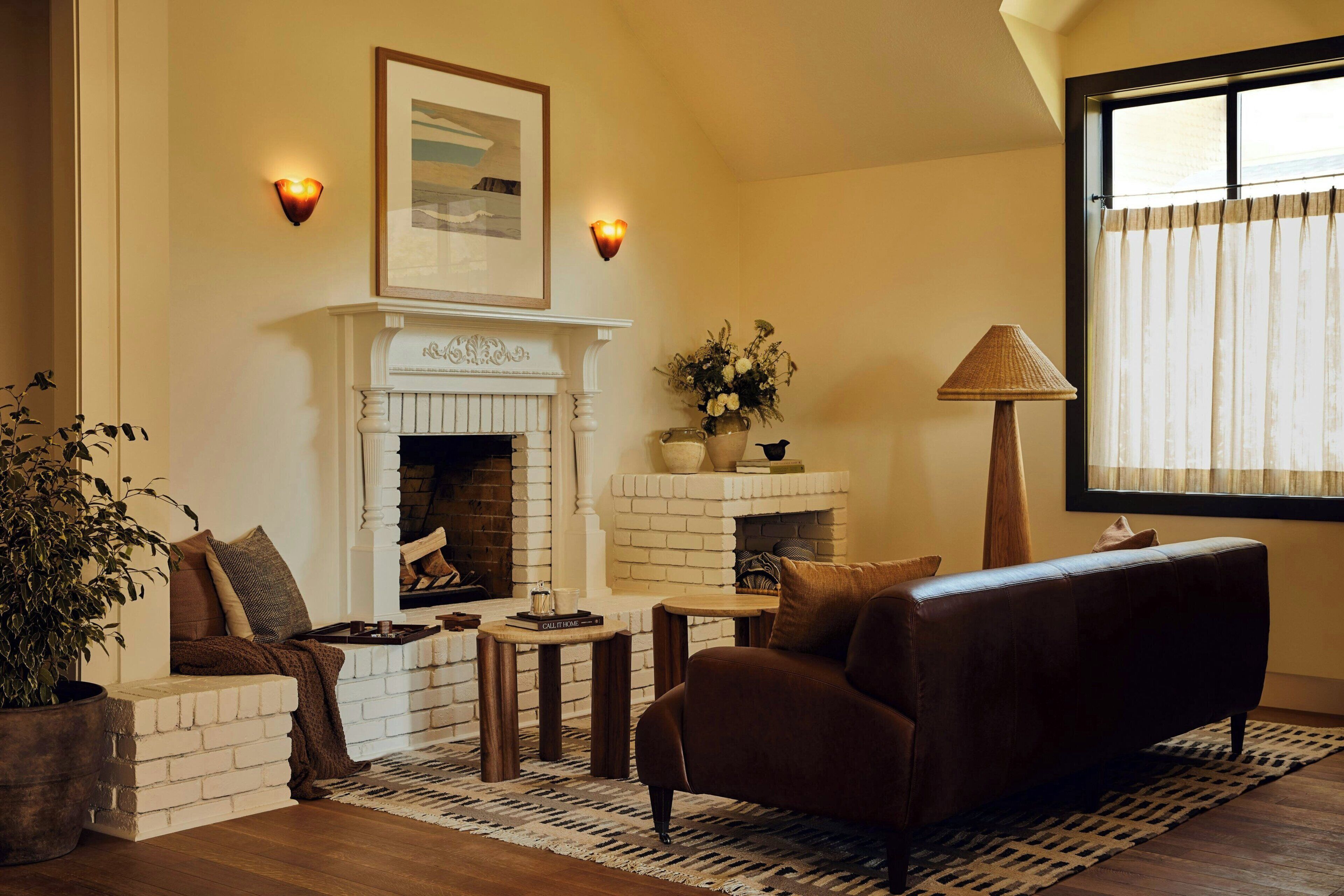 A cozy living room with a fireplace, a sofa, a coffee table, and a potted plant.