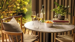 Una mesa redonda con dos copas de vino, una botella, un bol de aperitivos y un florero con flores.