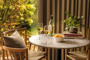 A round table with two wine glasses, a bottle, a bowl of snacks, and a vase with flowers. - Hill House at Trailborn Mendocino, Outdoor Collection by Marriott Bonvoy (Mendocino)