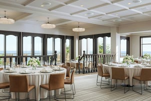 A restaurant with round tables set for dining, large windows with a view, and a ceiling with recessed lighting.