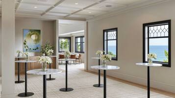 A hotel lobby with round tables, a painting, and a view of the sea.