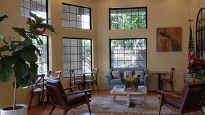 Amplia sala de estar con ventanas grandes, un sofá azul, muebles de madera y diversas plantas.
