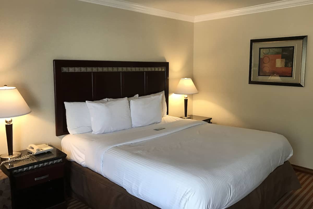 Ein Hotelzimmer mit einem großen Bett, zwei Nachttischlampen, einem Nachttisch mit Telefon und einem gerahmten Bild an der Wand.