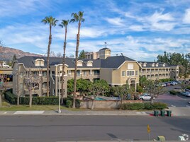 Un hotel de varios pisos con un patio central, palmeras y montañas al fondo.