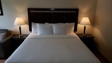 Una habitación de hotel con una cama grande, dos lámparas de noche, un cabecero y una mesita de noche con lámpara.
