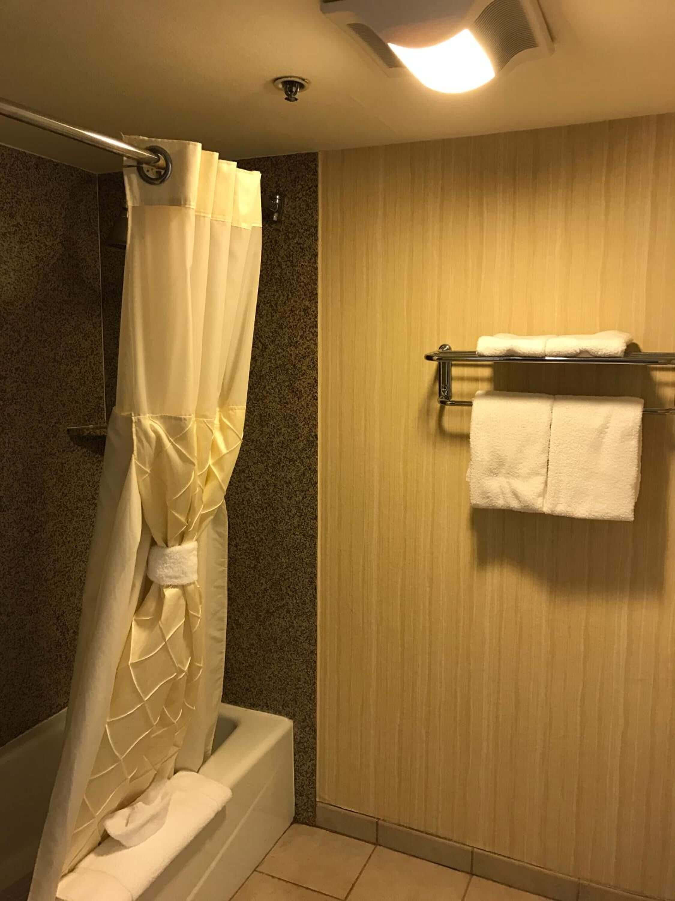 A bathroom with a shower curtain, a towel rack with two towels, and a wooden wall.