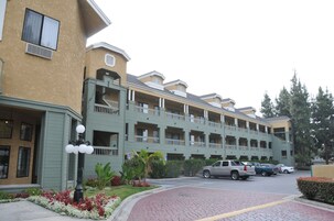 Un hotel de varios pisos con balcones, estacionamiento y un jardín ajardinado.