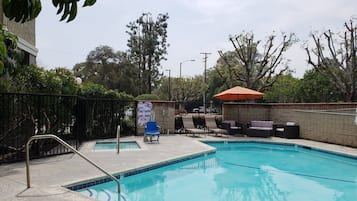 Una piscina con sillas de descanso y una sombrilla, rodeada de un muro de piedra y árboles.