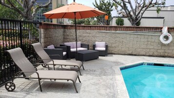Un área junto a la piscina con sillas de descanso y una mesa, una pared de piedra y un flotador salvavidas.