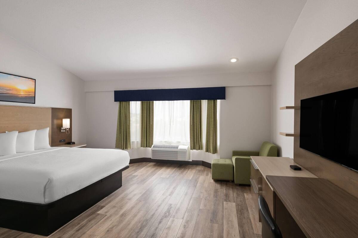 A modern hotel room with a large bed, a flat-screen TV, a desk, and a window with curtains.