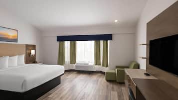 A modern hotel room with a large bed, a flat-screen TV, a desk, and a window with curtains.
