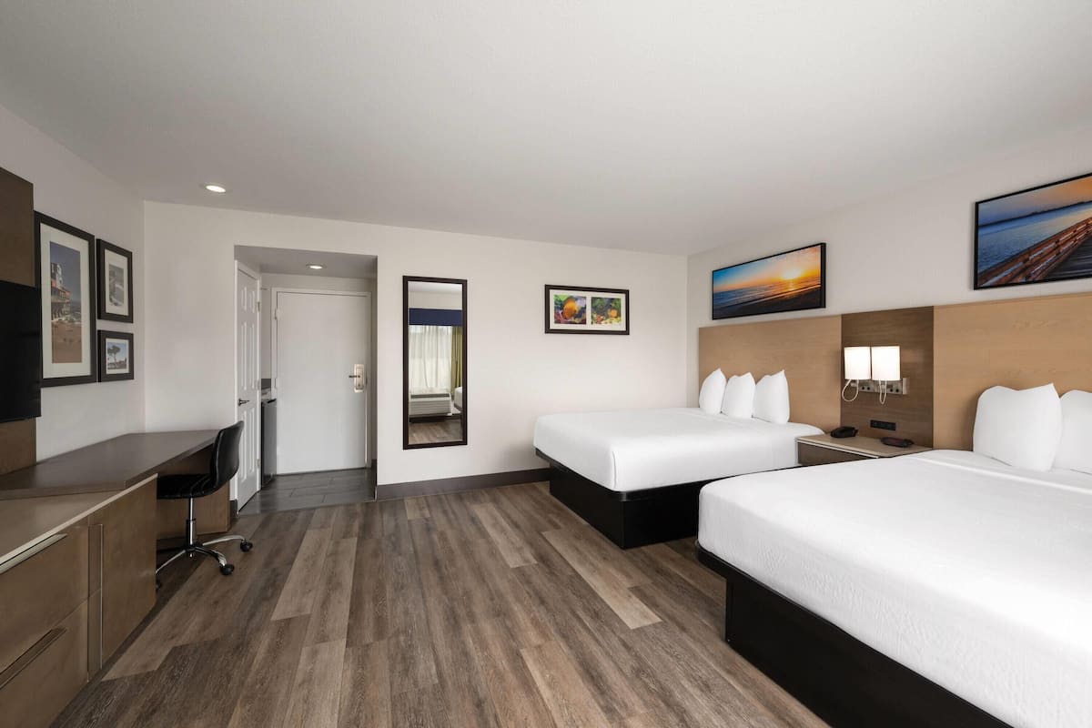 A hotel room with two beds, a desk, a chair, and a mirror.