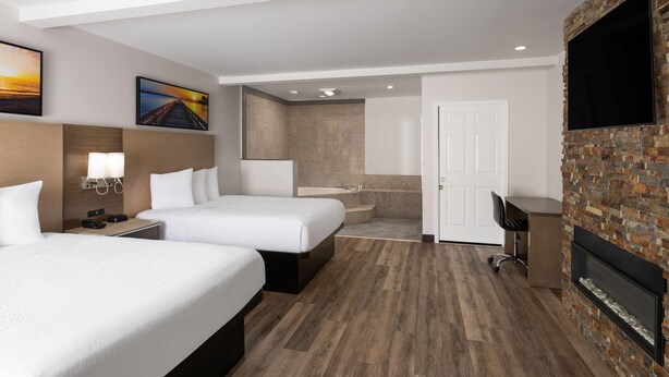 A hotel room with two beds, a desk, a TV, a fireplace, and a bathroom with a shower and sink. - Days Inn by Wyndham Monterey Downtown (Monterey)