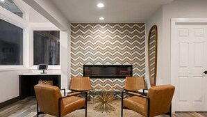 A modern living room with a large TV, two leather chairs, a glass coffee table, and a patterned wall. - Days Inn by Wyndham Monterey Downtown (Monterey)