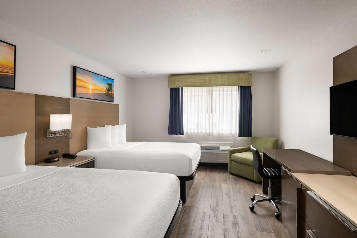 A hotel room with two beds, a desk, a chair, a TV, and a window with curtains.