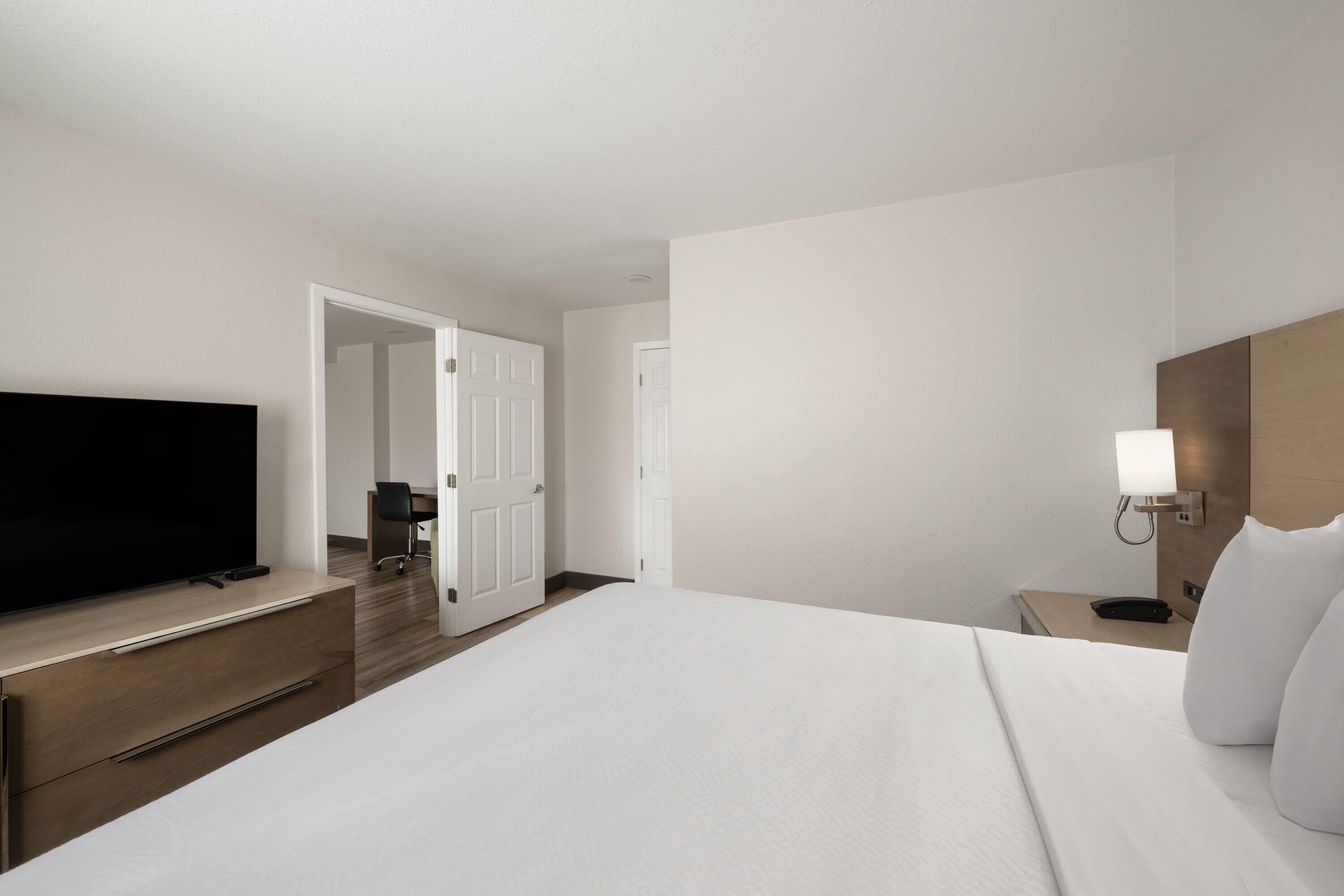 Habitación de hotel con una cama grande, un televisor de pantalla plana, una mesita de noche con lámpara y un aparador de madera.
