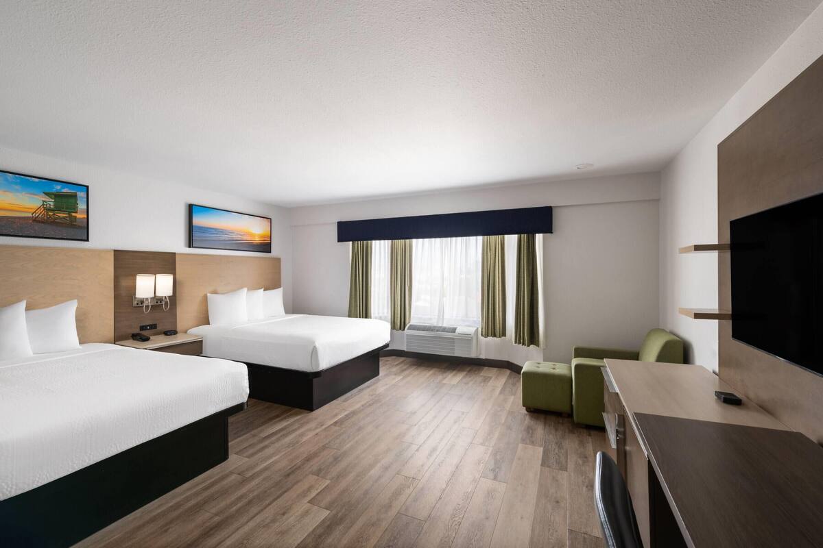 A hotel room with two beds, a desk, a chair, a TV, and a window with curtains.