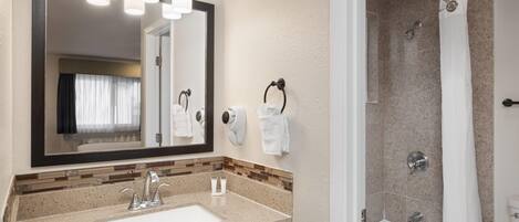 A bathroom with a sink, mirror, towel rack, and shower.