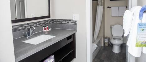 A bathroom with a sink, mirror, shower, toilet, and a towel rack.