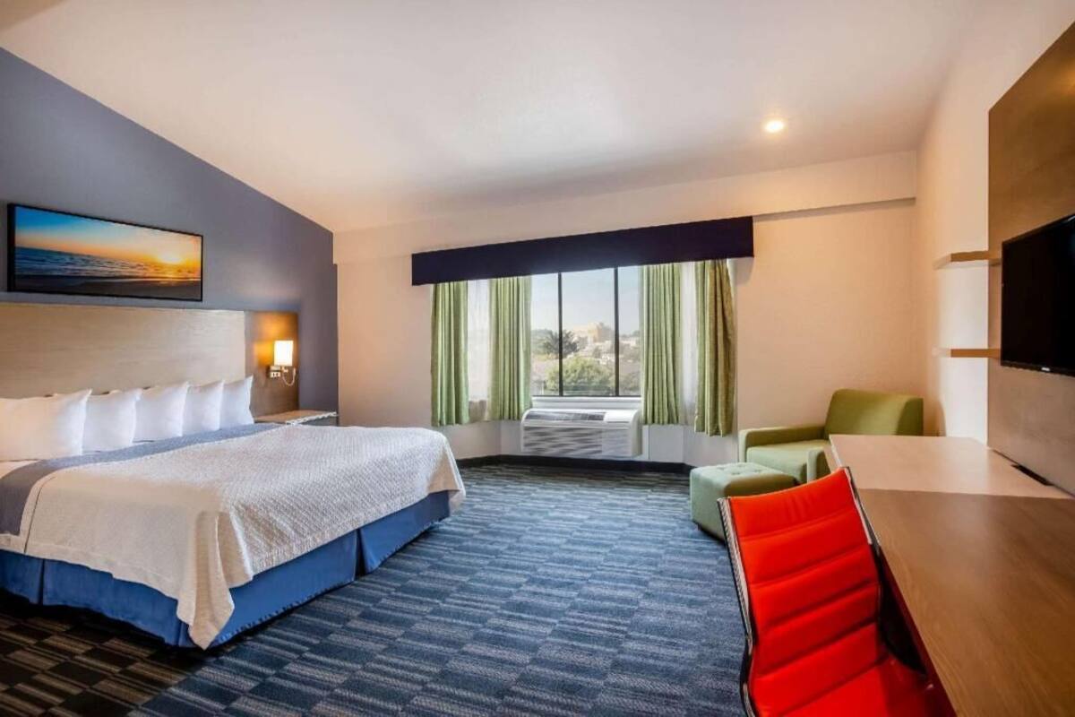 A hotel room with a bed, a desk, a chair, a TV, and a window with curtains.