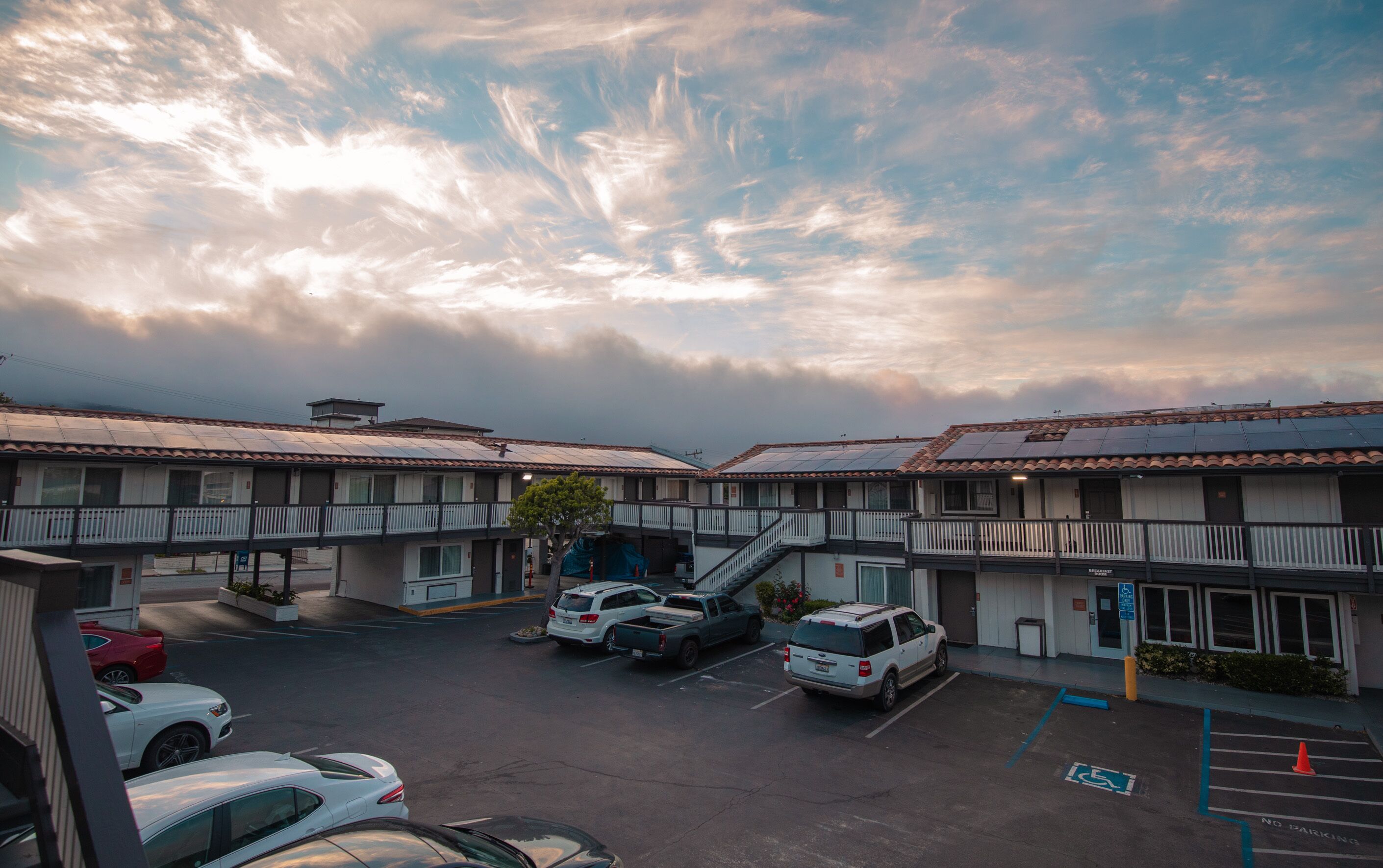 A motel with multiple units, a parking lot, and a clear sky with clouds.