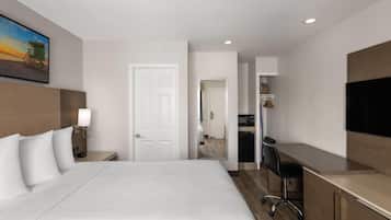 A hotel room with a large bed, a desk, a chair, a TV, and a door leading to a bathroom.