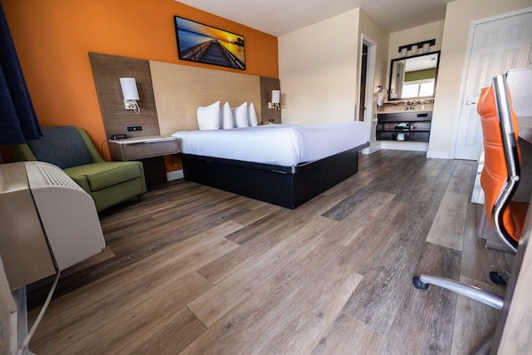 Quarto de hotel com cama, escrivaninha, cadeira, televisão e banheiro visível por uma porta aberta.