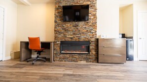 A modern living room with a stone fireplace, a flat-screen TV mounted above it, and a wooden cabinet to the right. - Days Inn by Wyndham Monterey Downtown (Monterey)