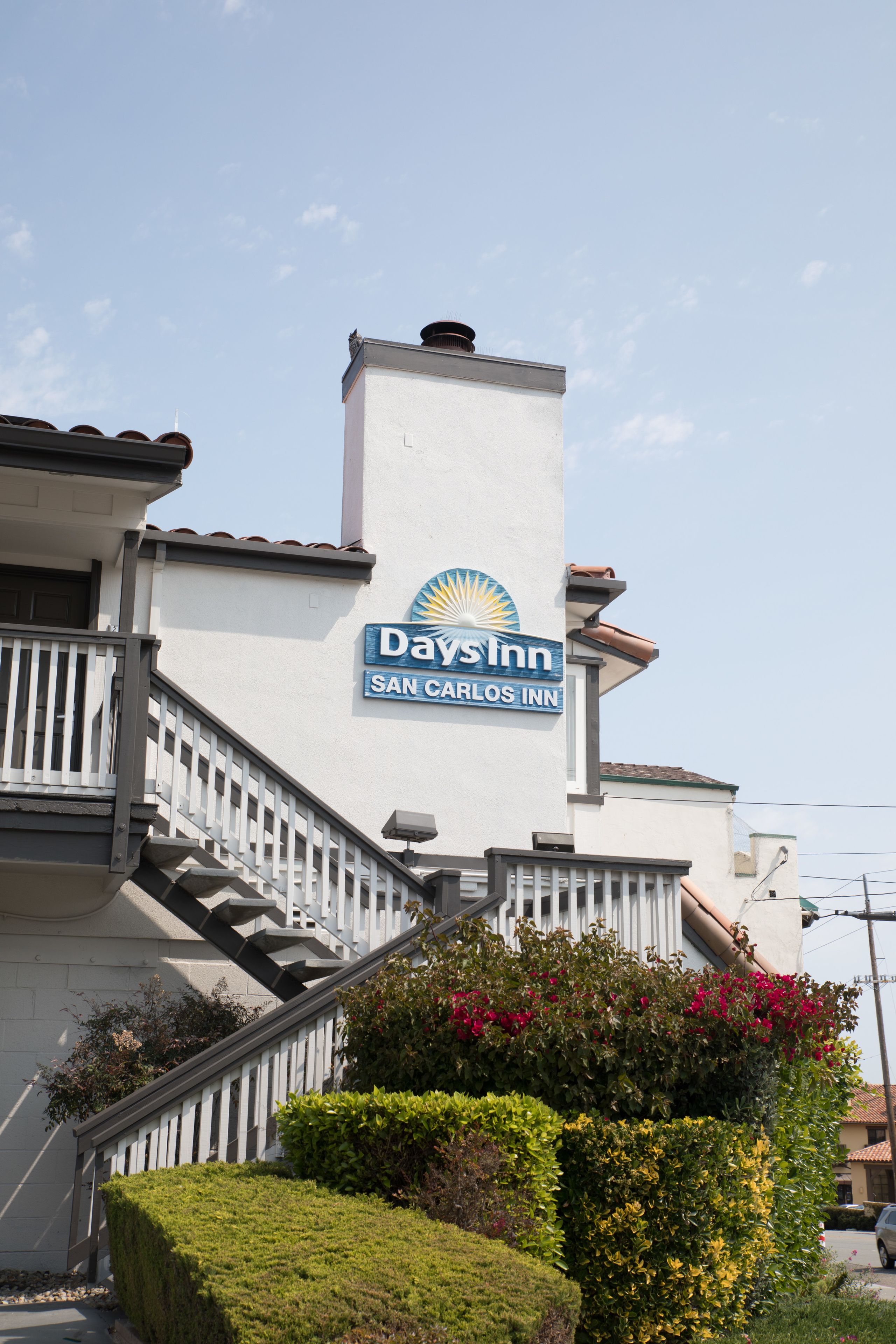 A Days Inn with a staircase leading to the entrance, surrounded by well-maintained hedges and flowering plants.