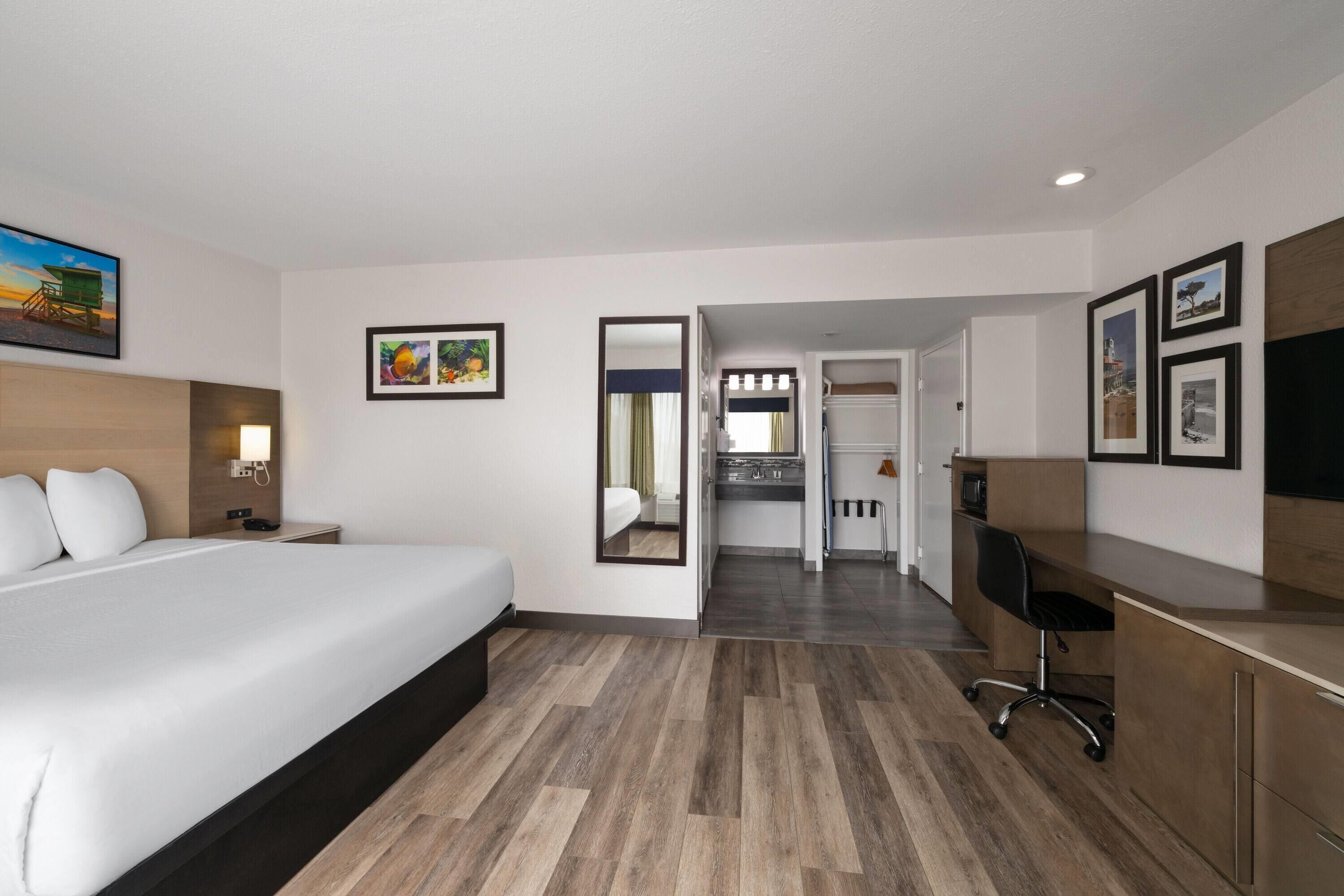 A hotel room with a bed, desk, and kitchenette.