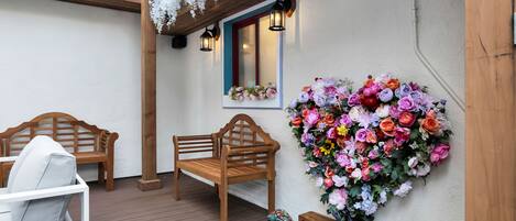 A wooden bench and a white chair under a wooden pergola with hanging white flowers.