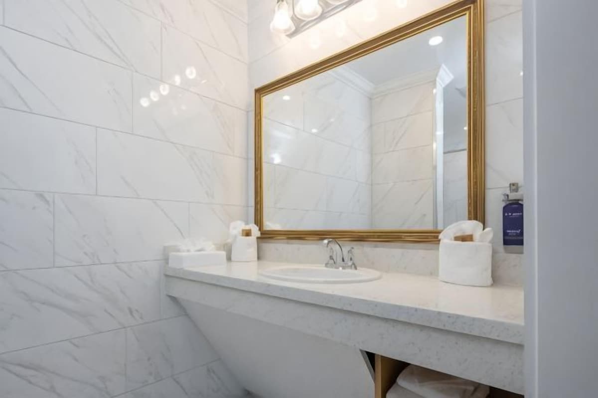 Une salle de bain avec un mur en marbre, un lavabo agrémenté d’un miroir à cadre doré et un porte-serviettes.