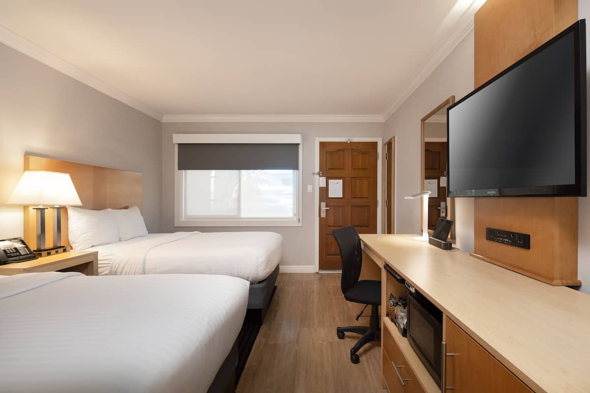 Habitación de hotel con dos camas, un escritorio, un televisor y una ventana con cortinas.