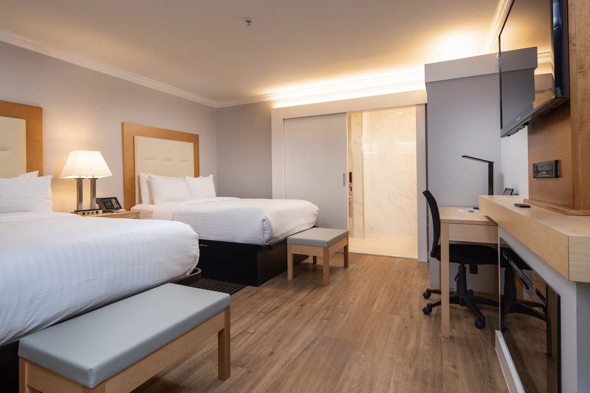 Habitación de hotel con dos camas, un escritorio, una silla, un banco, un televisor y un armario.