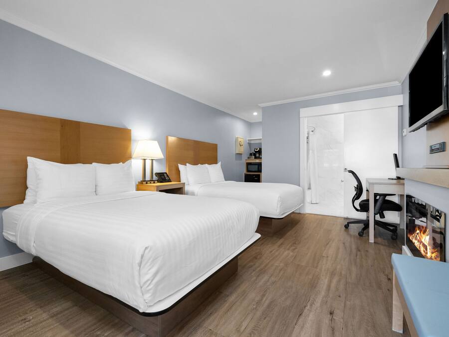 A hotel room with two beds, a desk, a TV, and a fireplace.