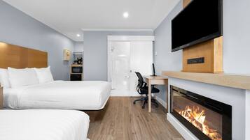 Quarto de hotel moderno com duas camas, TV, lareira e escrivaninha com cadeira.