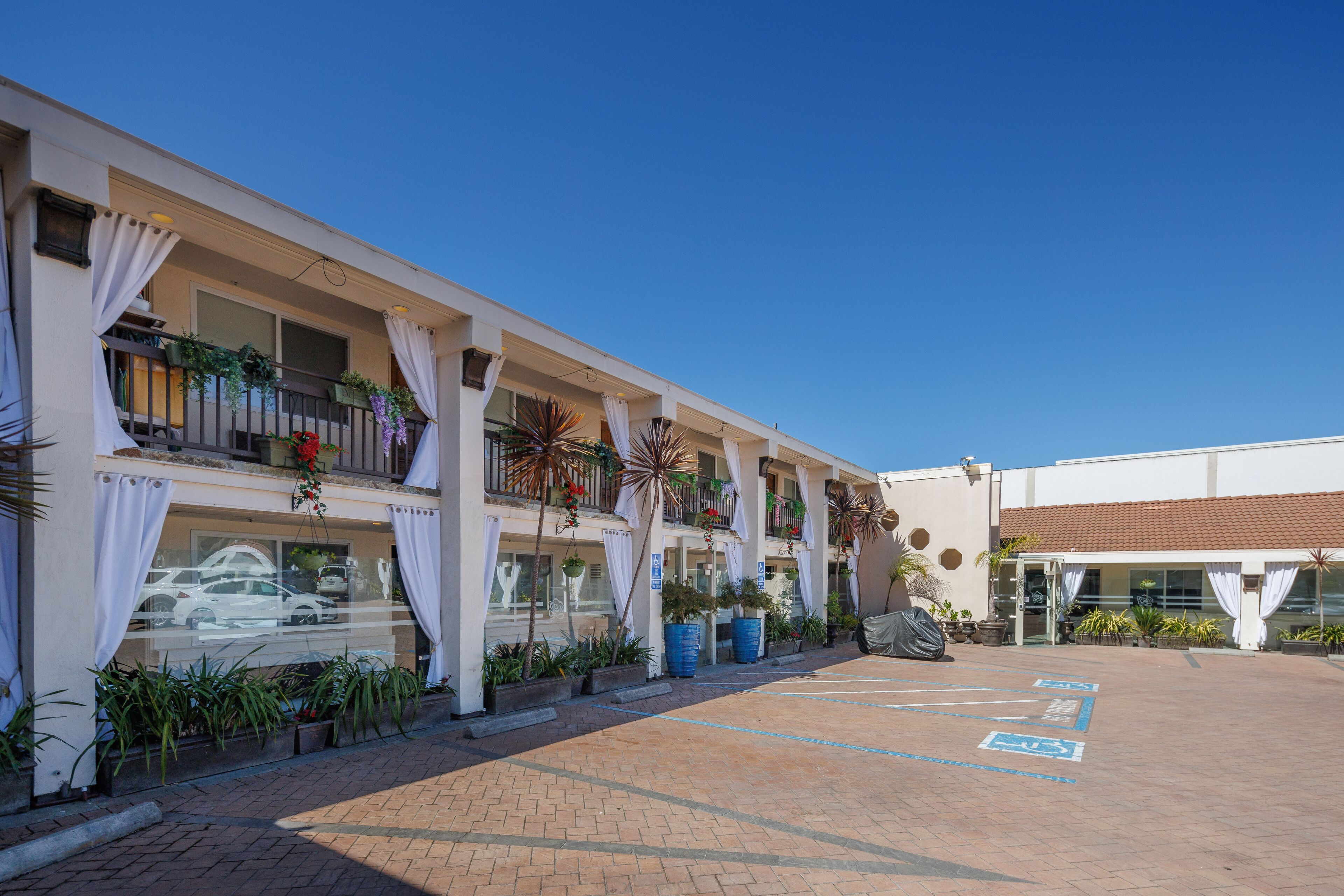 A hotel with a covered outdoor area, multiple balconies with plants, and a parking lot.
