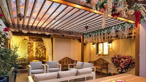 Un patio al aire libre con mobiliario de madera, luces colgantes y adornos florales.