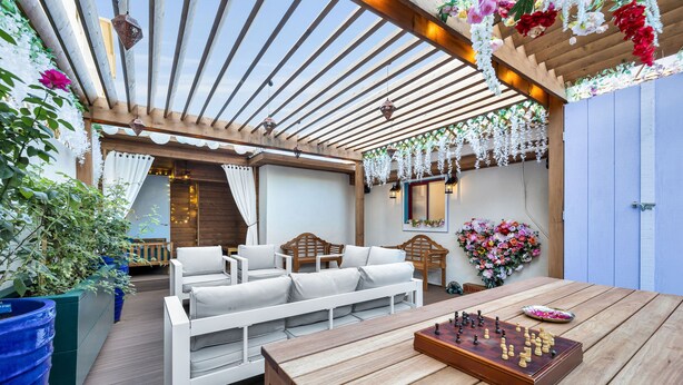 Un patio al aire libre con mobiliario de madera, un tablero de ajedrez y decoraciones florales colgantes.