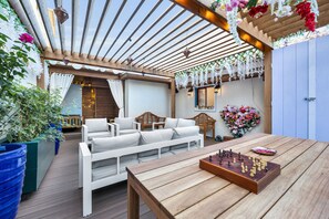 Eine Terrasse im Freien mit Holzmöbeln, einem Schachbrett und hängenden floralen Dekorationen.