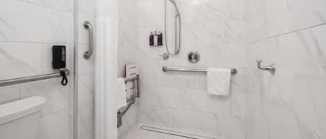 Een moderne badkamer met witte marmeren tegels, een toilet, een douche met handgrepen en een handdoekhouder.