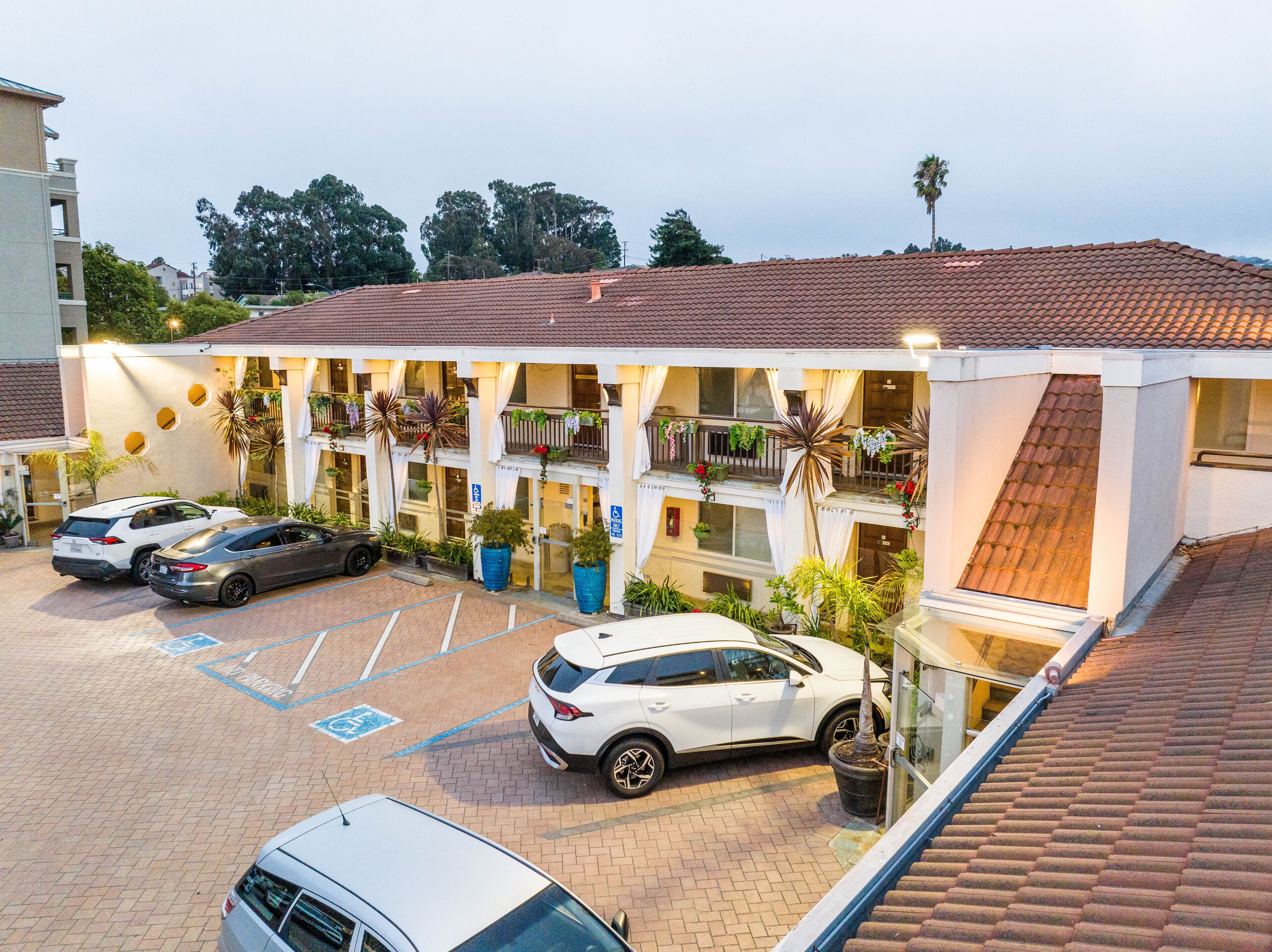 A hotel with a parking lot, multiple floors, and balconies with plants.